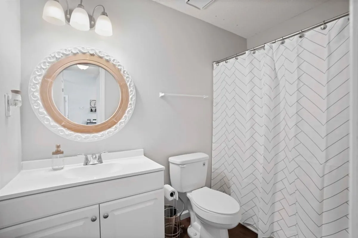 A fresh, modern bathroom featuring a round mirror, vanity sink, and a stylish shower curtain. The space feels clean and inviting, ideal for personal grooming and relaxation.