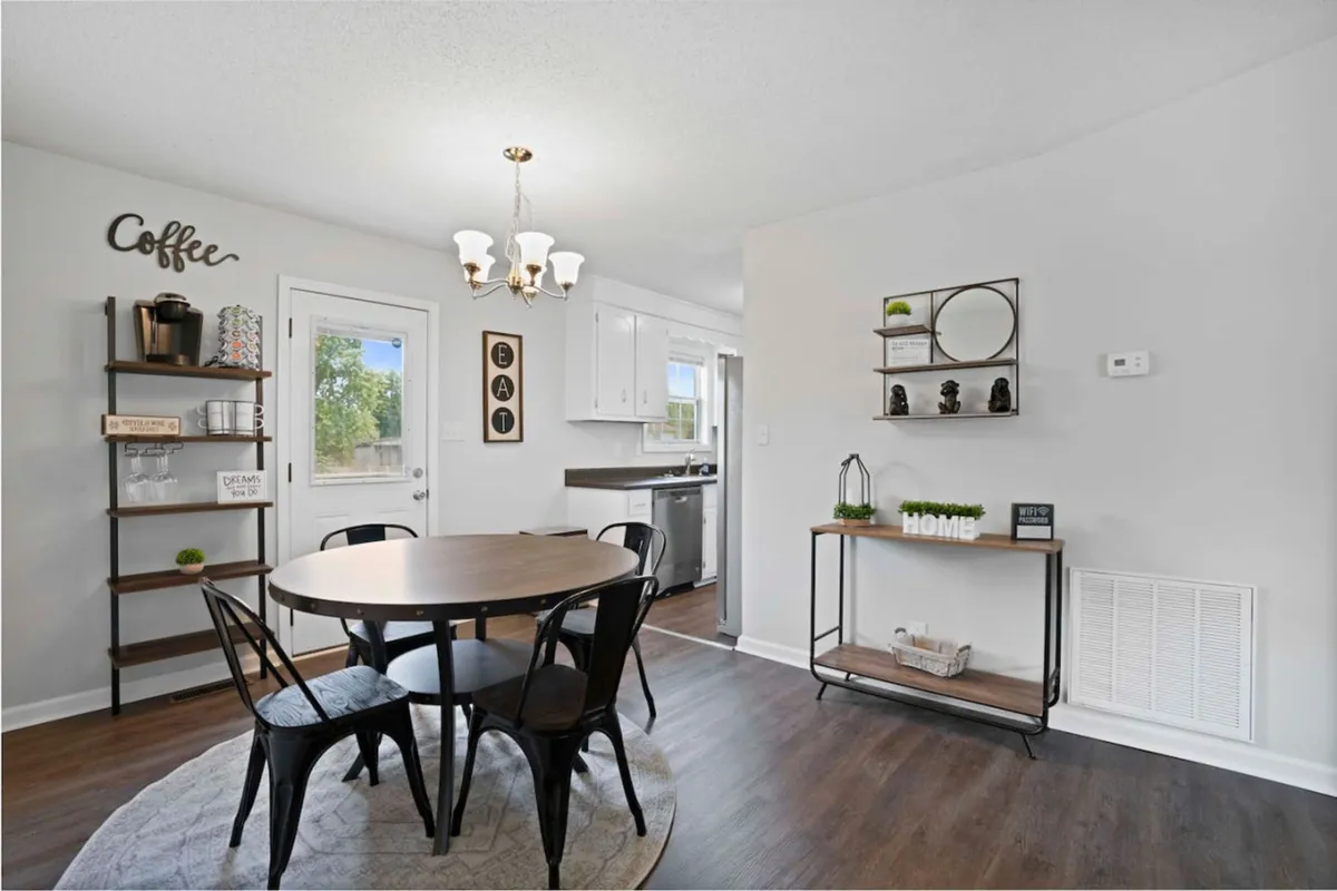 A round dining table set near shelves with tasteful decor, with the kitchen entrance visible in the background. The space is bright and arranged for family meals, casual coffee gatherings, or conversations before heading out for a day of adventure.