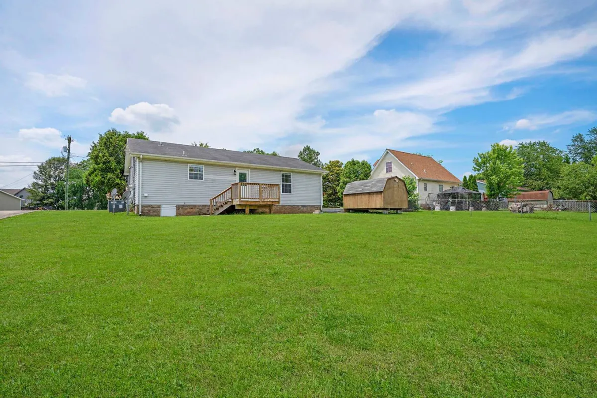 A backyard scene focused on a wooden deck attached to the house, with a storage shed visible in the background and well-maintained landscaping. The setting radiates calm, perfect for watching sunsets or hosting an intimate gathering on the patio.