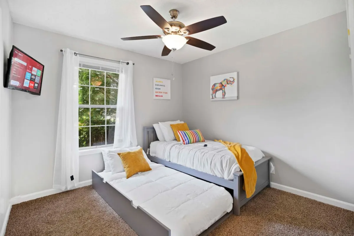 A cheerful bedroom with a bunk bed dressed in colorful throw pillows, a television, and playful details. Natural light fills the space, making it inviting for both rest and play.