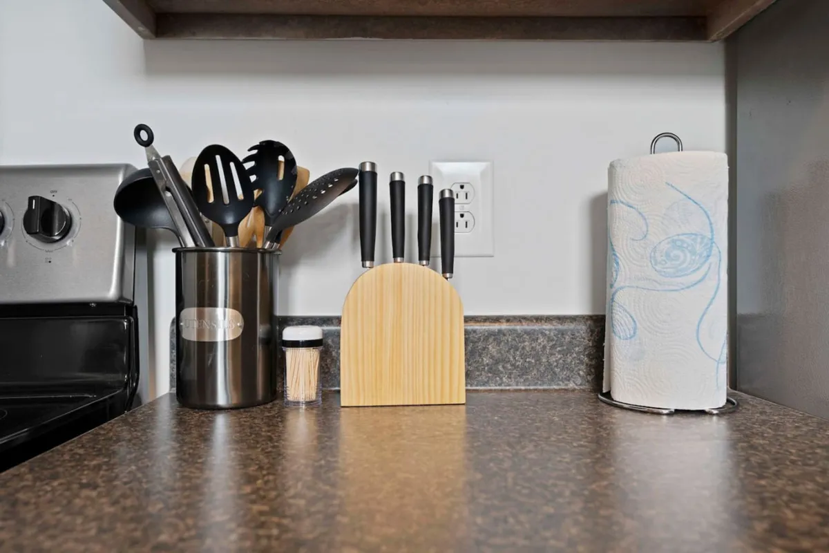 A functional kitchen scene focusing on a knife block, utensil holder, and paper towel dispenser, representing essential cookware and utensils for meal preparation.