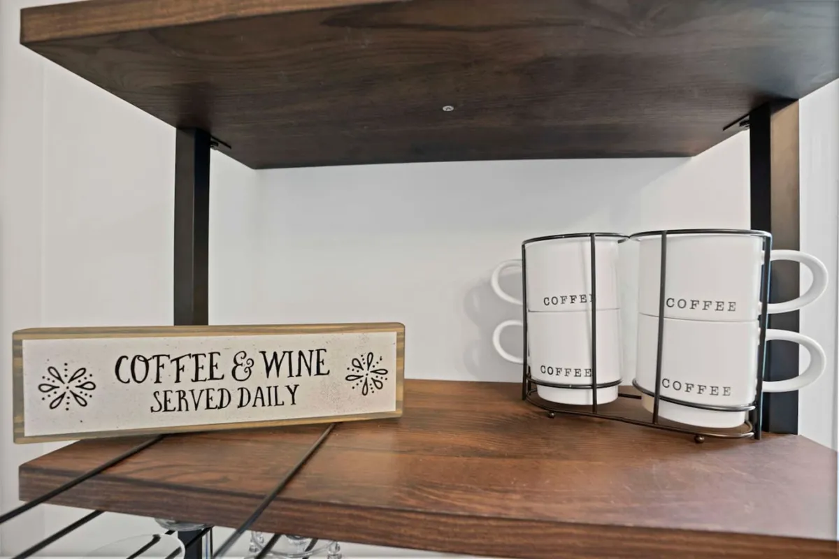 A close-up view features a 'coffee and wine' sign hung above a stack of coffee mugs, suggesting a cozy corner dedicated to morning brews or evening wine. The ambiance is friendly and inviting, perfect for couples to start or end their day together.