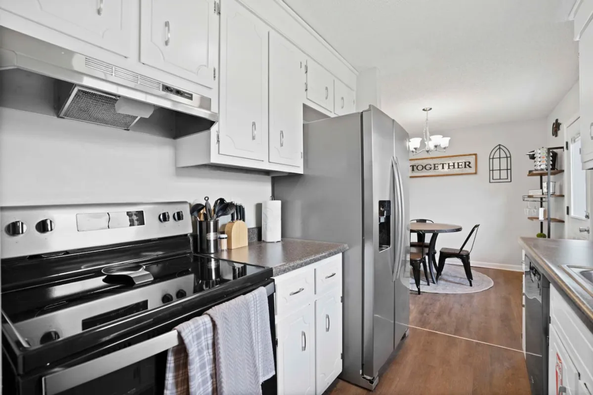 This image showcases a kitchen space with gleaming stainless steel appliances, bright white cabinetry, and a view of a dining area in the background. The space appears modern and functional, offering both cooking and communal dining experiences.