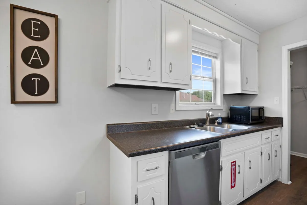 A close-up of kitchen countertops, featuring a sink and dishwasher, with framed wall art providing a welcoming atmosphere. The ample counter space is noticeable, supporting cooking or meal prep activities.